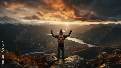 Man raises one hand punching the air on mountain peak with sunset background