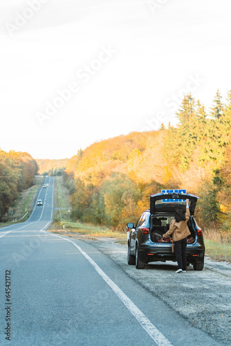 A woman who parked in the autumn forest on the side of the road opens the trunk of her car.