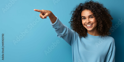 a young woman pointing on a plain blue background, fashio