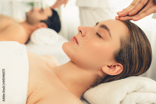 Caucasian couple enjoying relaxing anti-stress head massage and pampering facial beauty skin recreation leisure in dayspa modern light ambient at luxury resort or hotel spa salon. Quiescent