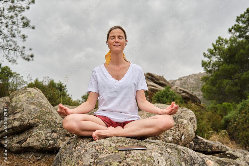 A Woman meditating in easy pose while sitting on rock