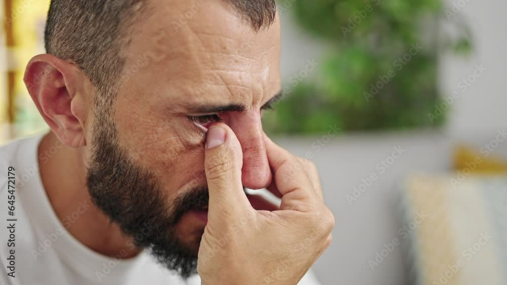 Young hispanic man crying sitting on the sofa at home