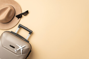 Autumn adventure aspirations. Top view photograph capturing a gray suitcase, a warm felt hat, and sunglasses displayed on beige isolated backdrop, well-suited for your advertising or textual purposes