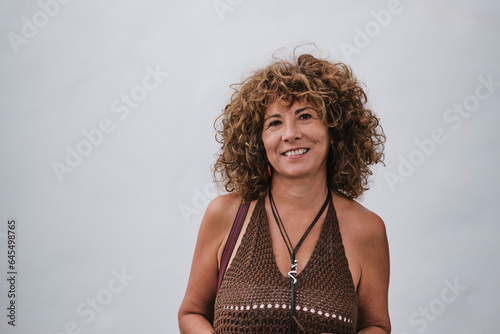 Middle-aged Hispanic woman with wavy hair smiling in front of white wall