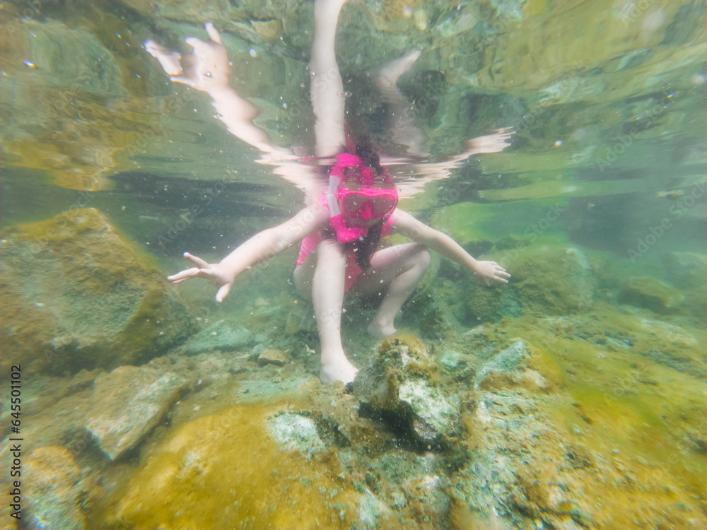 Fototapeta premium Underwater photo, a small child girl in a pink swimsuit with a snorkel and diving mask is snorkeling at the Rummu quarry.