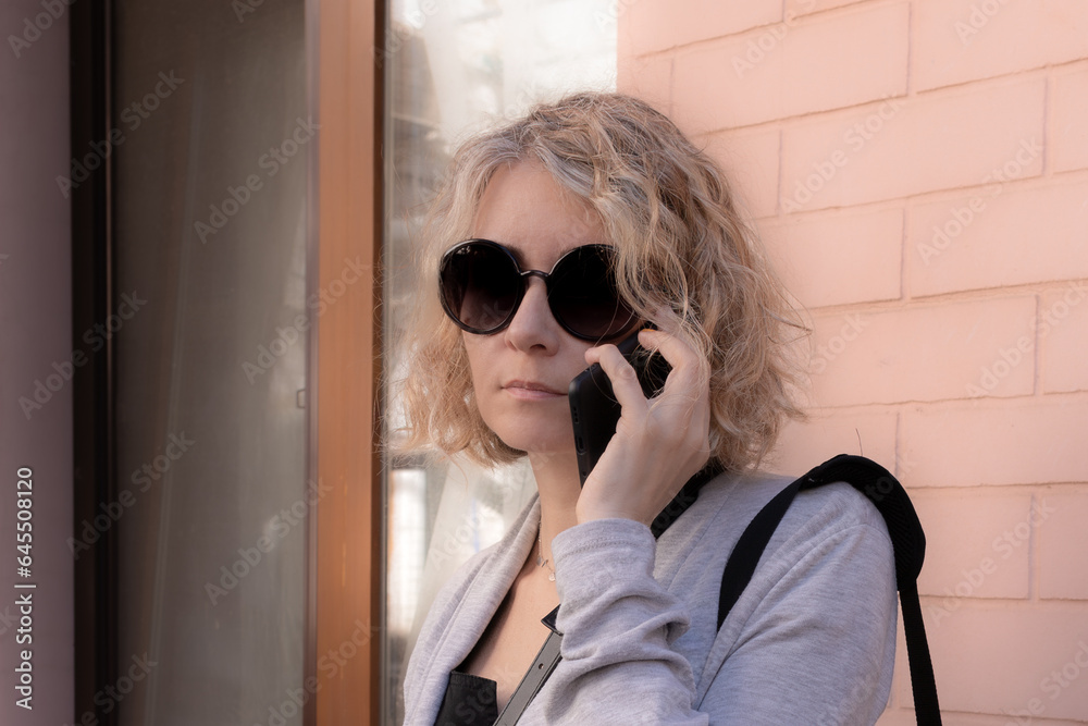 Beautiful young woman. A stranger with a phone. Unknown girl. Light curls. Voluminous hairstyle. Blonde in sunglasses. City life. Clothing style. Talk on the telephone. Beautiful young woman. A stranger with a phone. Unknown girl. Light curls. Voluminous hairstyle. Blonde in sunglasses. City life. Clothing style. Talk on the telephone.