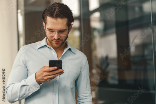 Smiling businessman holding phone while standing in office during break time. High quality photo