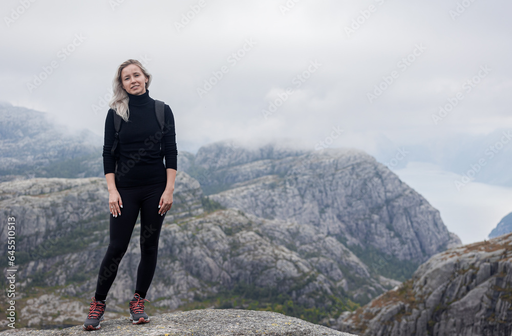 a girl with a backpack standing on the rock in the mountains on a hike in Norway on fjord