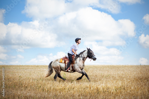 A young teenage girl gallops on a horse across a field, against the backdrop of a cloudy sky. Horse riding, horse riding, horse riding lessons. © наталья саксонова