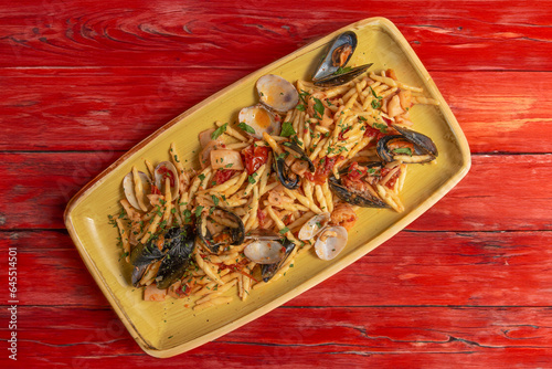 italian homemade pasta called trofie ai frutti di mare with tomatoes, mussels, clams, prawns, on the other hand, horizontal on shabby red wooden table