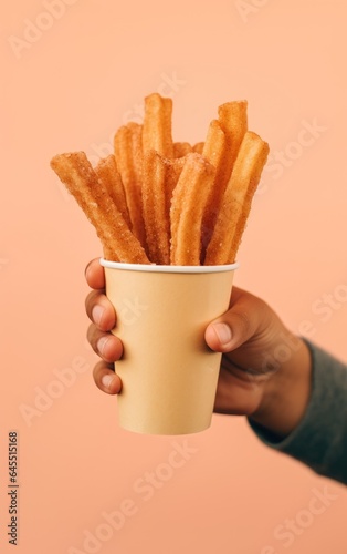 Churros traditional Spain or Mexican street fast food, baked snack made from sweet dough in a paper cup in hand