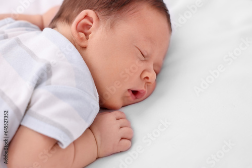 Cute newborn baby sleeping on white bed, closeup. Space for text