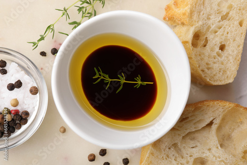 Bowl of organic balsamic vinegar with oil and spices served with bread slices on beige table, flat lay
