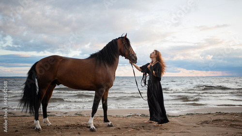 beautiful young rider in a dress and with her hair down, leads her horse along the beach. horseback riding in the open air