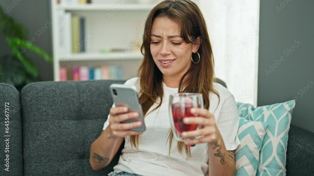 Young beautiful hispanic woman using smartphone sitting on sofa surprised at home Young beautiful hispanic woman using smartphone sitting on sofa surprised at home