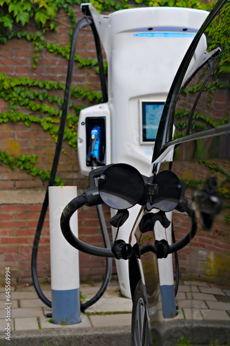 Electric car connected with cable and plug to the EV charging station for recharge vehicle battery, in the background a wall with hedra ivy for green clean environment concept
