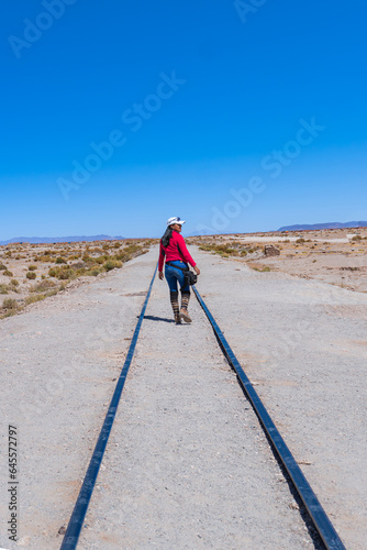 Fashion meets nature: young woman in a red outfit in the Uyuni, Bolivia railway desert.