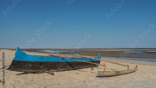 Homemade blue and black wooden boat on the sand at low tide of the ocean. Puddles of water are visible in the distance. Clear blue sky. Madagascar. Mozambique Channel. Morondava