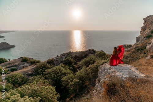 Woman sunset sea red dress, back view a happy beautiful sensual woman in a red long dress posing on a rock high above the sea on sunset.