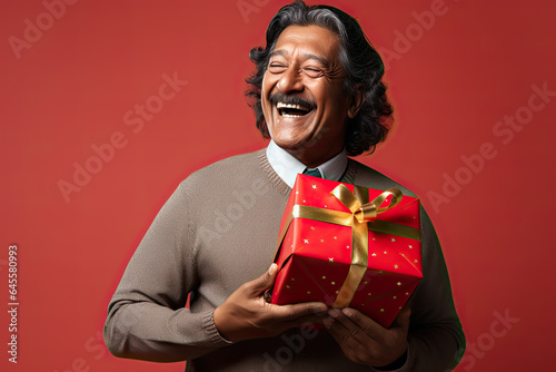 Portrait of a middle-aged Indian male with a gift box, on a red background © Lucy Welch