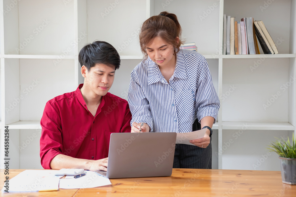 Cheerful business people using a laptop in an office. Happy young entrepreneurs smiling while working together in a modern workspace. Two young business people are sitting together at a table. Cheerful business people using a laptop in an office. Happy young entrepreneurs smiling while working together in a modern workspace. Two young business people are sitting together at a table.
