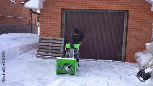 A man cleans snow in the winter in the courtyard of the house.  man cleaning snow with a snow blower