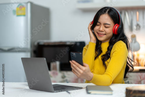 Cheerful Asian woman in headset laughing happily Listen to music, relax, use your laptop, stream video conference calls, teach online. hobby ideas work from home © Phimwilai