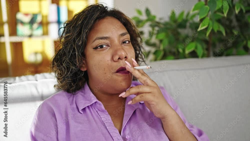 Young beautiful latin woman sitting on sofa smoking cigarette smiling at home Young beautiful latin woman sitting on sofa smoking cigarette smiling at home