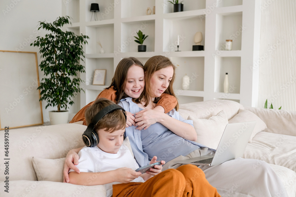 Young mother working on laptop in living room with her children playing around. Woman Freelancer, parenting or working from home concept. Business from distance and virtual communication. Young mother working on laptop in living room with her children playing around. Woman Freelancer, parenting or working from home concept. Business from distance and virtual communication.