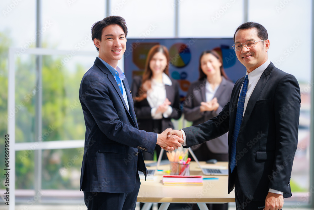 Fototapeta premium Two Asian Business Professionals Shaking Hands in Office, Celebrating a Successful Corporate Agreement