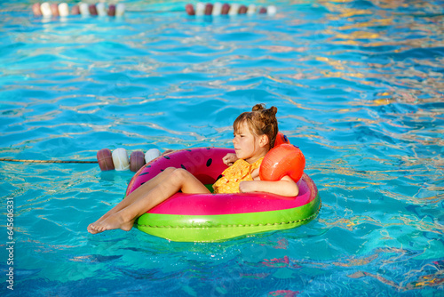Happy little girl with inflatable toy ring float in swimming pool. Little preschool child learning to swim and dive in outdoor pool of hotel resort. Healthy sport activity and fun for children.