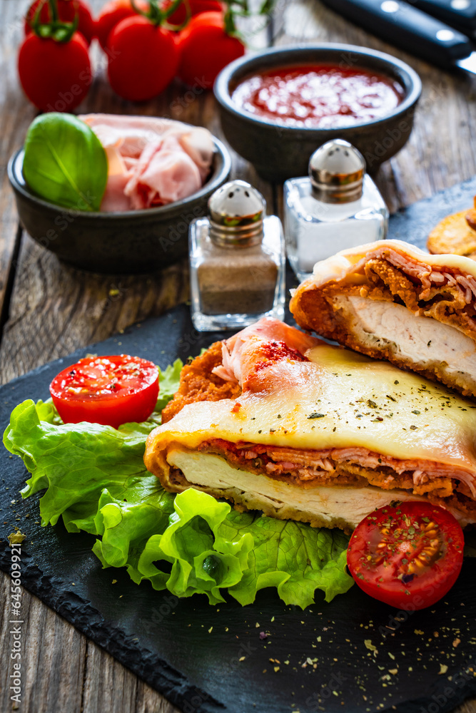Milanesa Napolitana - fried breaded cutlet with ham, mozzarella cheese and tomato sauce on wooden background
