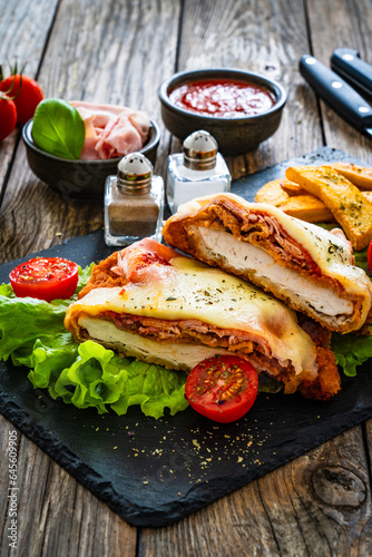 Milanesa Napolitana - fried breaded cutlet with ham, mozzarella cheese and tomato sauce on wooden background 