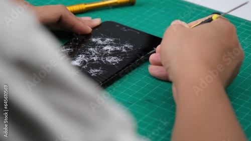 Close up hands of a service worker repairing modern smartphone. Smartphone with cracked display and screwdrivers. Smartphone damage, touch screen scratched with spider web.