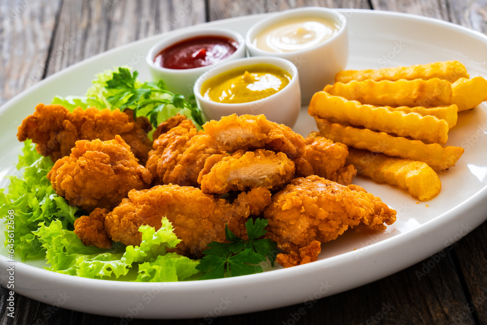Seared breaded chicken nuggets with French fries on wooden table
Seared breaded chicken nuggets with French fries on wooden table