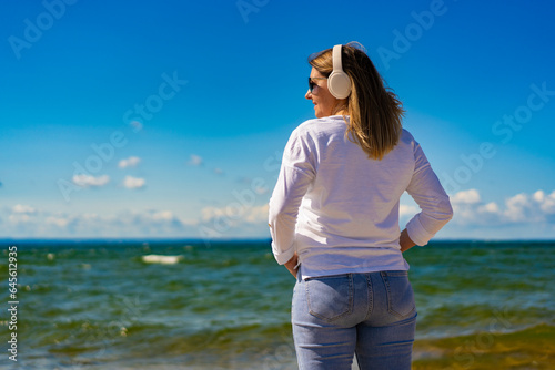 Beautiful woman walking on sunny beach listening to music 