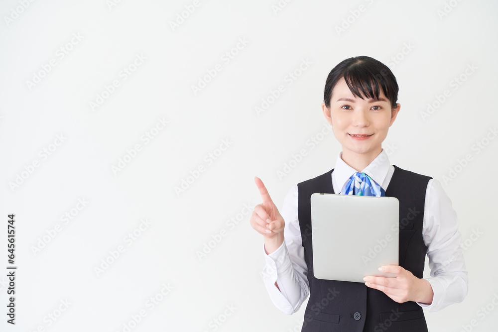 タブレットを操作するベストにリボンタイの制服を着た、受付業務、事務業務の女性 タブレットを操作するベストにリボンタイの制服を着た、受付業務、事務業務の女性