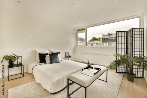 a bedroom with white walls and wood flooring in the room  there is a large window that looks out onto the street