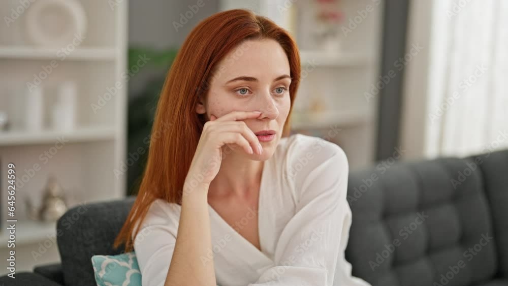 Young redhead woman sitting on sofa with serious expression at home Young redhead woman sitting on sofa with serious expression at home