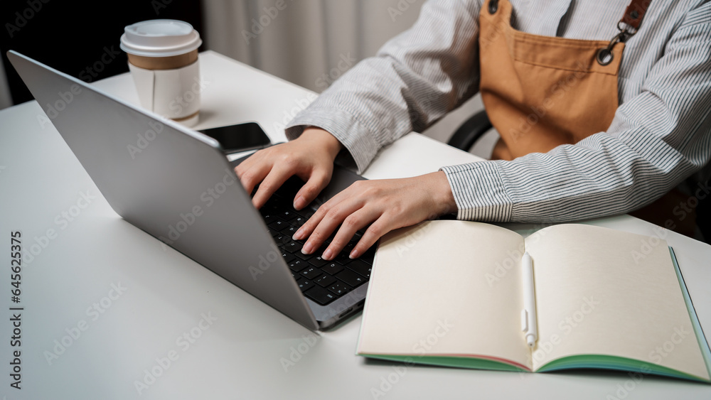 Hands typing on laptop computer keyboard for mockup multimedia technology device phone, notebook, coffee on table indoor workspace working business owner meeting online at home or shop wearing apron Hands typing on laptop computer keyboard for mockup multimedia technology device phone, notebook, coffee on table indoor workspace working business owner meeting online at home or shop wearing apron