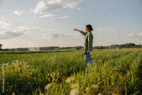 Smiling female farmer standing on the field and pointing at side on gorizont. Agricultural concept