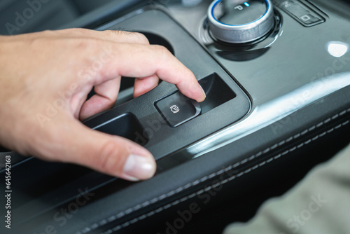 Action of a car driver is using finger to activate the eletrical parking brake system by pulling the button. Transporation equipment object photo, selective focus. photo