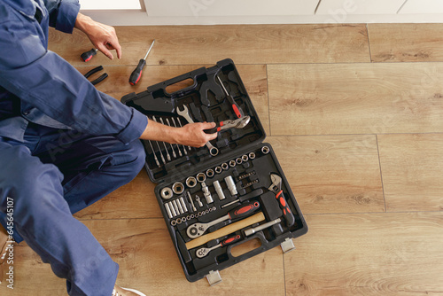 Top view of professional handyman with open tool bag sitting on home kitchen floor  photo