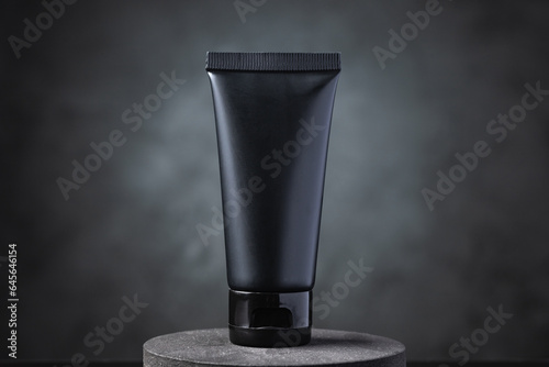 Black cosmetic squeeze tube on black circular podium. © Thitiwat.Day