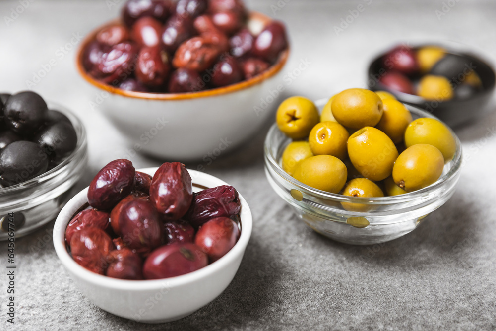 A set of green, red and black olives on a marble background. Various types of olives in bowls and fresh olive leaves. Vegan. Olive fruits. Place for text. Copy space.