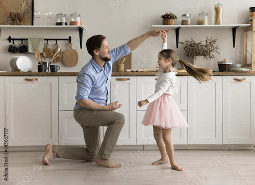 Happy loving daddy dancing with little princess daughter kid, holding hand of girl wearing pink ballet skirt, spinning around with flying hair, training choreograpgy, playing active game