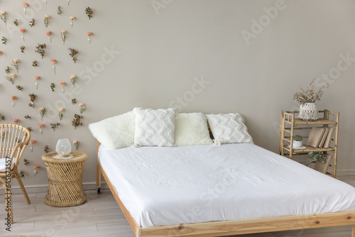 Wooden double bed with comfortable orthopedic mattress, white sheet, cushions in eco interior design. Stylish modern empty bedroom with no people, natural decoration, bamboo furniture