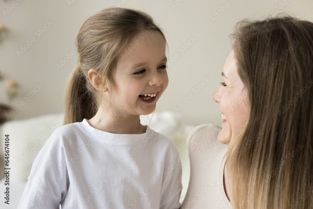 Happy mom and cheerful cute toddler girl relaxing at home, sitting close, talking, laughing, having fun. Positive loving mother enjoying motherhood, family leisure with sweet little child