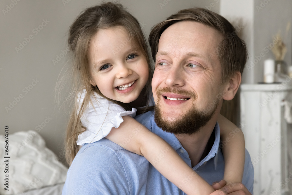 Happy loving father playing funny games with cute toddler daughter at home, holding little child on back, piggybacking kid. Sweet girl hugging dad at home, looking at camera, smiling Happy loving father playing funny games with cute toddler daughter at home, holding little child on back, piggybacking kid. Sweet girl hugging dad at home, looking at camera, smiling