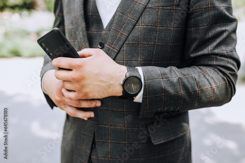 Portrait, close-up photo of a man, a businessman in a gray plaid suit with a phone, a smartphone and a wristwatch on his hand. Business, lifestyle.